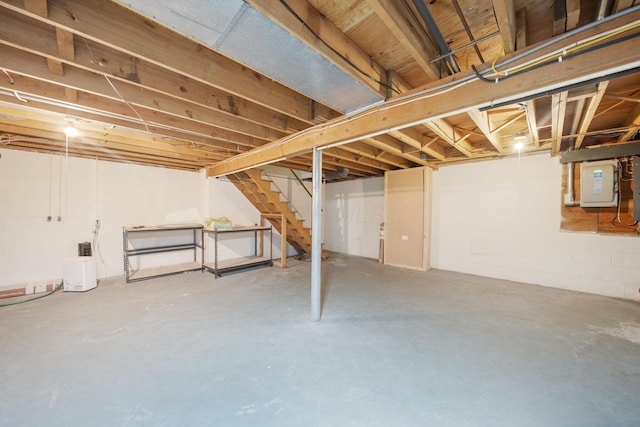 unfinished basement with electric panel, concrete block wall, and stairs