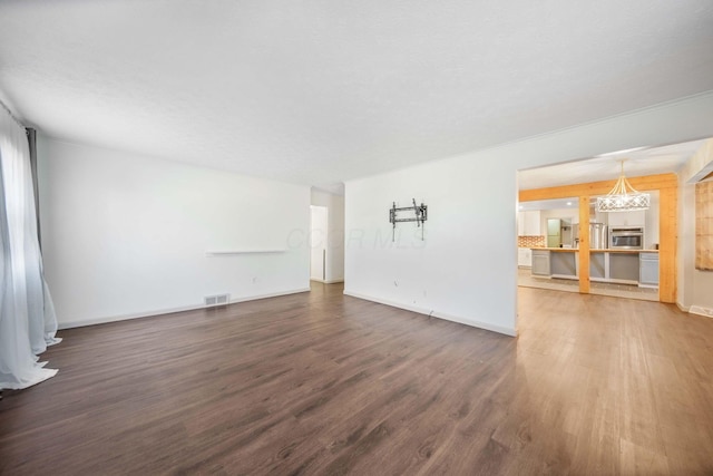 unfurnished living room featuring a notable chandelier, wood finished floors, visible vents, and baseboards