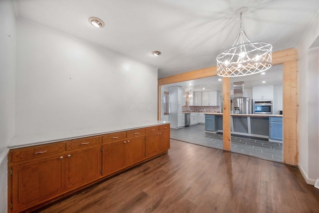 kitchen featuring dark wood finished floors, decorative backsplash, brown cabinets, a notable chandelier, and stainless steel appliances