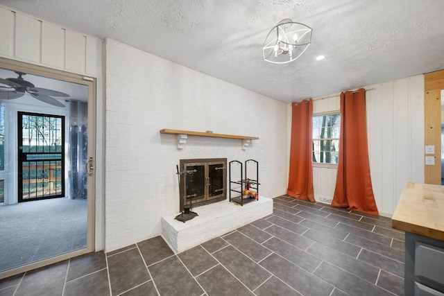 unfurnished living room featuring brick wall, ceiling fan, a fireplace, a textured ceiling, and dark tile patterned flooring