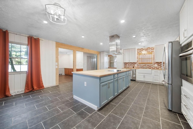 kitchen with a center island, appliances with stainless steel finishes, wall chimney exhaust hood, butcher block counters, and white cabinets