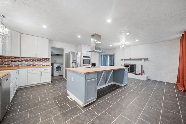 kitchen featuring ventilation hood, appliances with stainless steel finishes, white cabinets, butcher block counters, and washer / dryer