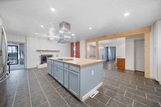 kitchen with a kitchen island with sink, wood counters, a glass covered fireplace, open floor plan, and wall chimney exhaust hood