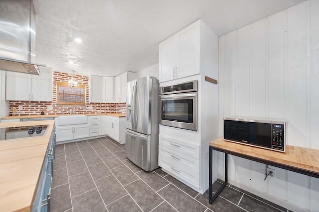 kitchen featuring a sink, white cabinetry, appliances with stainless steel finishes, exhaust hood, and butcher block counters