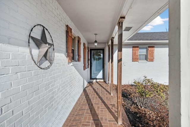 doorway to property featuring visible vents, brick siding, and a shingled roof