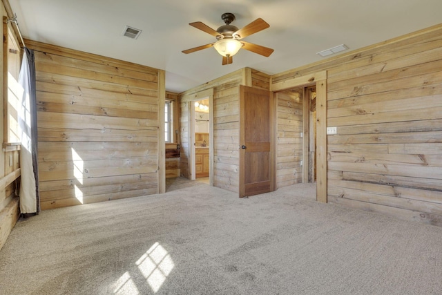 unfurnished bedroom featuring ensuite bathroom, visible vents, carpet floors, and wood walls