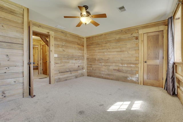 carpeted spare room with visible vents, wood walls, and a ceiling fan