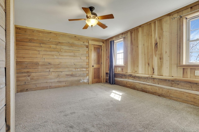 spare room with a wealth of natural light, carpet, wood walls, and ceiling fan