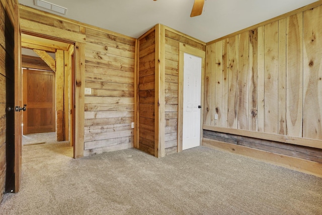 unfurnished bedroom featuring visible vents, wood walls, ceiling fan, and carpet floors