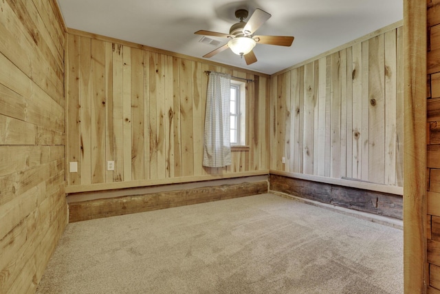 carpeted spare room featuring wooden walls, visible vents, and ceiling fan