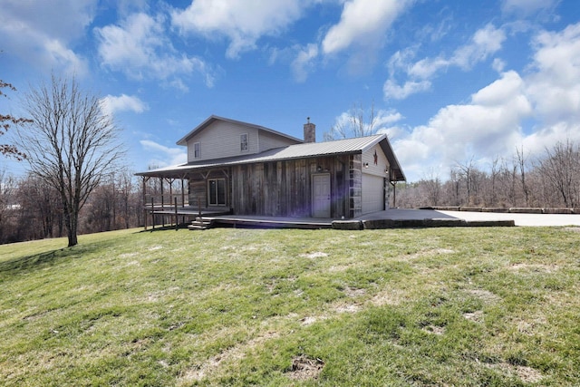 back of property featuring a yard, metal roof, concrete driveway, a garage, and a chimney