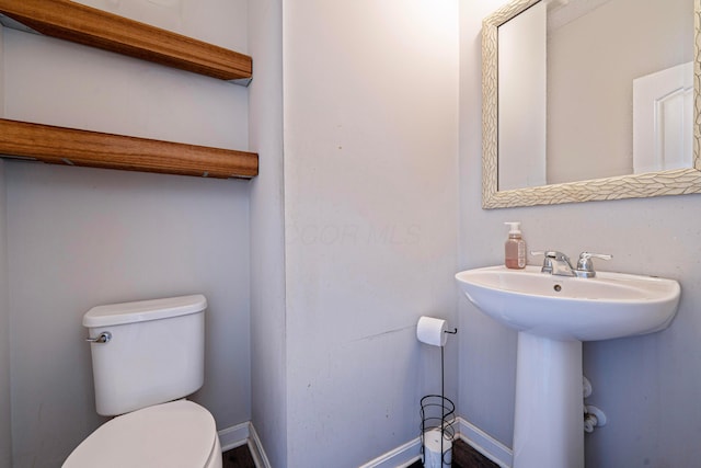 half bath with toilet, baseboards, and a sink