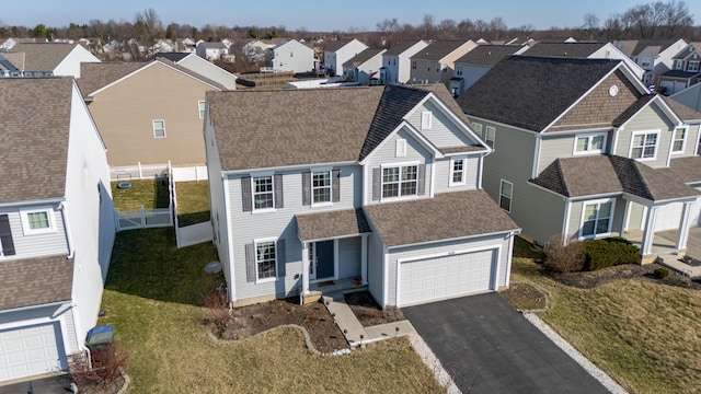 view of front of house with driveway, fence, a residential view, an attached garage, and a shingled roof