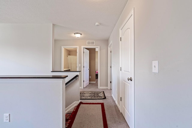 hall featuring baseboards, light colored carpet, visible vents, and a textured ceiling