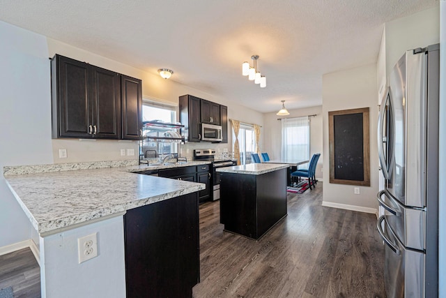 kitchen with dark wood-type flooring, a kitchen island, appliances with stainless steel finishes, a peninsula, and light countertops