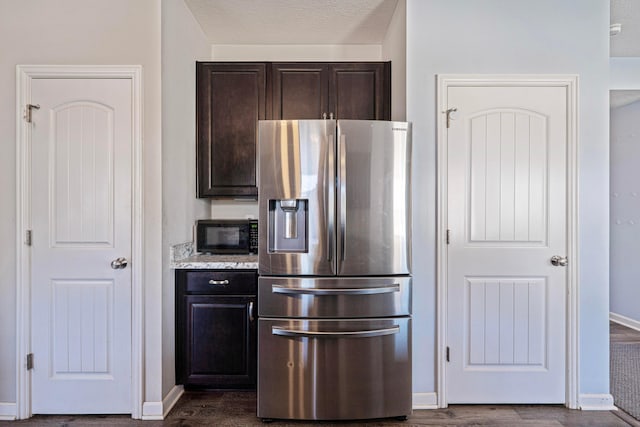 kitchen featuring a textured ceiling, black microwave, stainless steel fridge with ice dispenser, baseboards, and dark brown cabinets