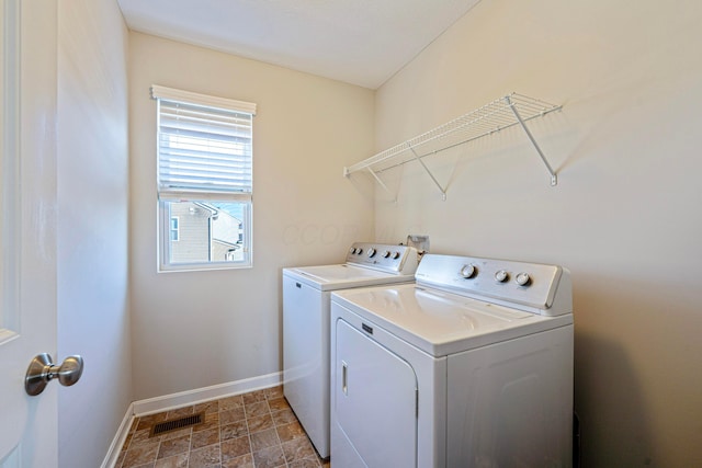 laundry room with baseboards, visible vents, laundry area, stone finish floor, and washer and clothes dryer