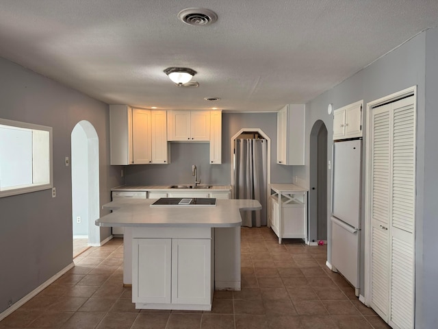 kitchen featuring white cabinets, arched walkways, freestanding refrigerator, and a sink