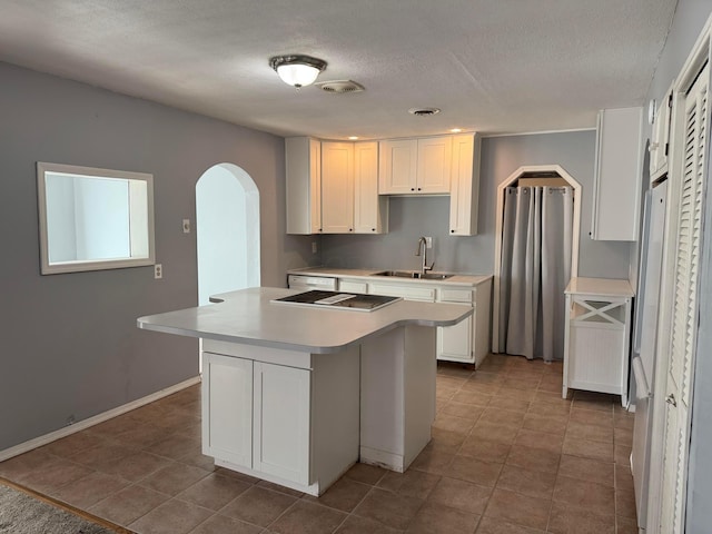 kitchen with a sink, a kitchen island, white cabinetry, arched walkways, and light countertops