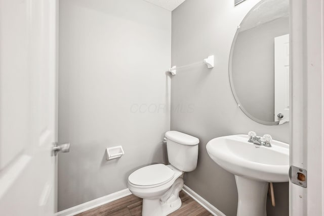 bathroom with toilet, baseboards, and wood finished floors