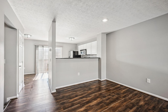 kitchen with stainless steel microwave, dark wood finished floors, decorative backsplash, freestanding refrigerator, and white cabinetry