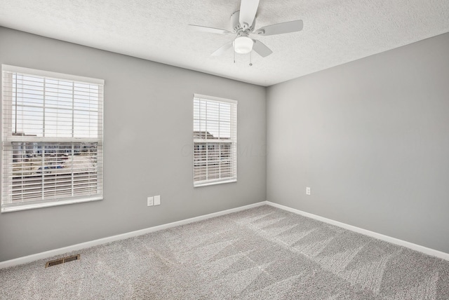 unfurnished room with a ceiling fan, carpet, visible vents, baseboards, and a textured ceiling