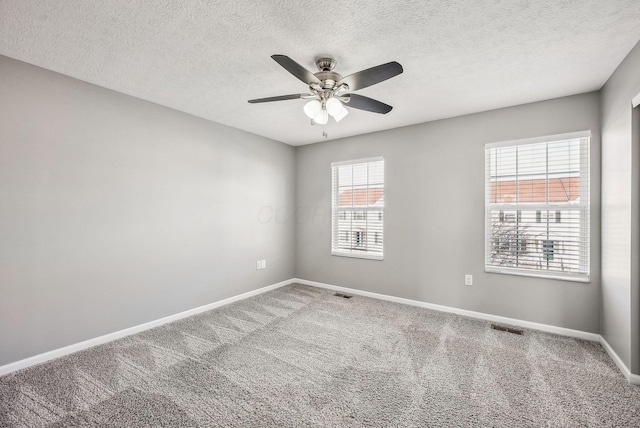 carpeted spare room with visible vents, baseboards, a textured ceiling, and a ceiling fan