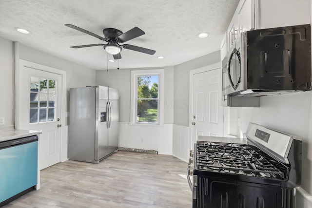 kitchen featuring light wood-style flooring, wainscoting, white cabinets, appliances with stainless steel finishes, and a textured ceiling