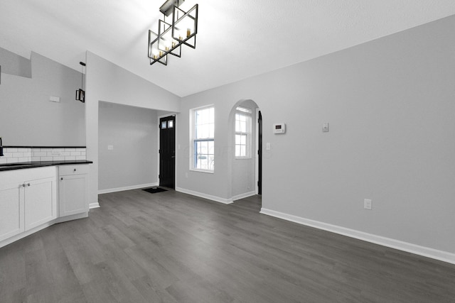 interior space with dark wood-style floors, arched walkways, vaulted ceiling, white cabinetry, and dark countertops