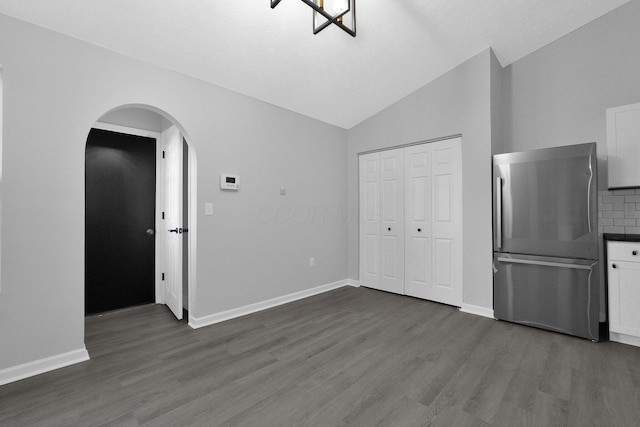 interior space with arched walkways, dark wood-style floors, baseboards, and vaulted ceiling