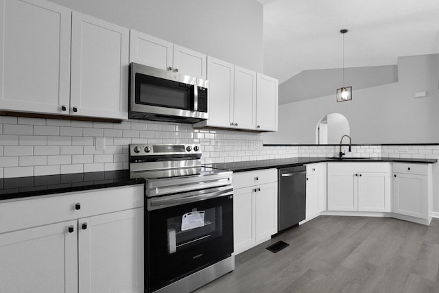 kitchen with a sink, lofted ceiling, dark countertops, and appliances with stainless steel finishes