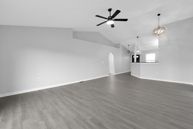 unfurnished living room with lofted ceiling, ceiling fan with notable chandelier, dark wood-style floors, arched walkways, and baseboards