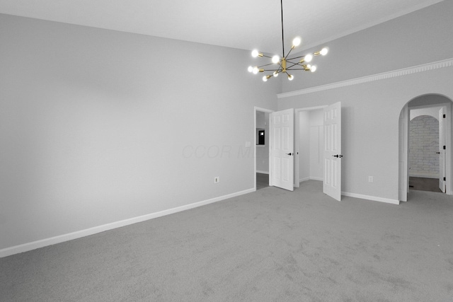 carpeted spare room featuring baseboards, arched walkways, and a chandelier