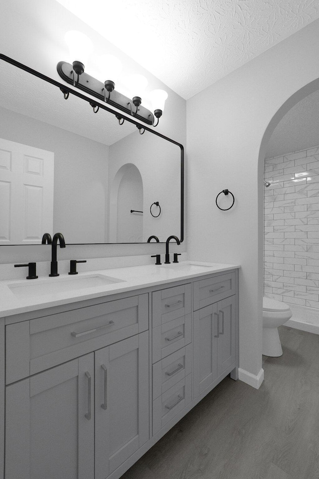 bathroom featuring a textured ceiling, double vanity, wood finished floors, and a sink