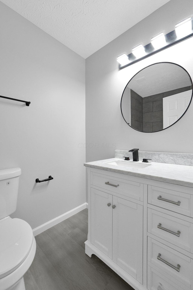 bathroom featuring toilet, a textured ceiling, wood finished floors, baseboards, and vanity