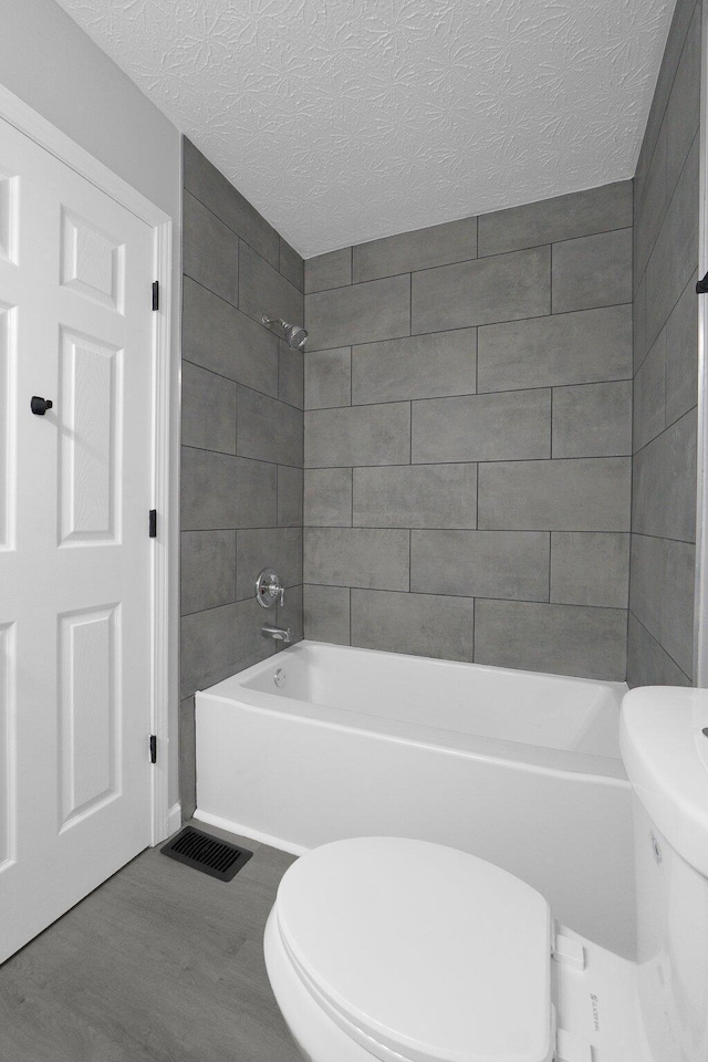 bathroom with visible vents, toilet, a textured ceiling, shower / washtub combination, and wood finished floors