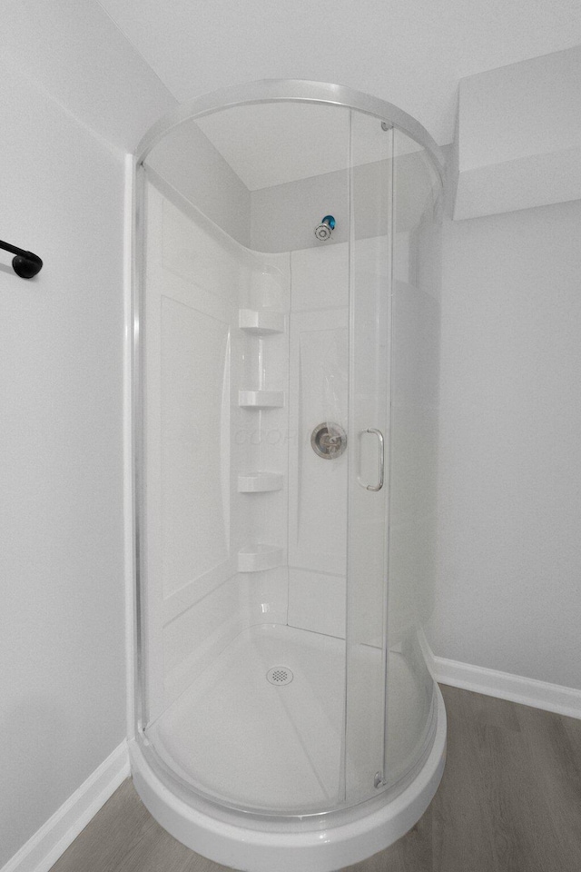 full bath featuring a stall shower, baseboards, and wood finished floors