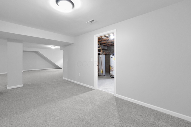 finished basement with visible vents, baseboards, carpet flooring, and water heater