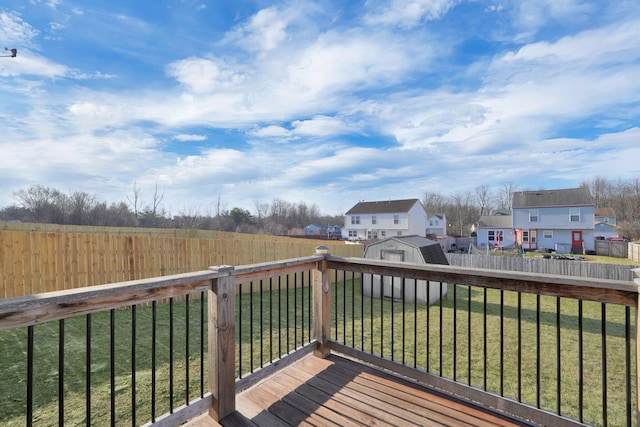 wooden terrace featuring a residential view, a lawn, a fenced backyard, an outbuilding, and a storage unit