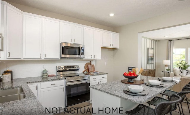 kitchen with light stone counters, appliances with stainless steel finishes, a breakfast bar area, and white cabinetry