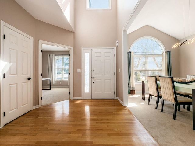 entrance foyer featuring light carpet, light wood-style flooring, baseboards, and a towering ceiling