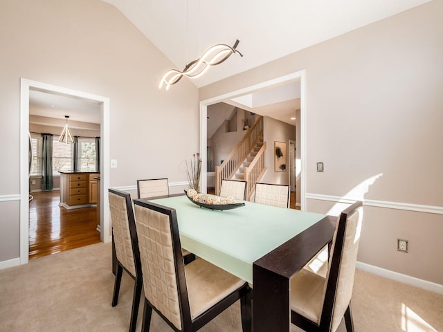 dining room featuring stairway, light colored carpet, baseboards, and high vaulted ceiling