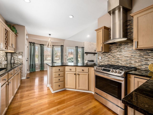 kitchen featuring light brown cabinetry, light wood-style floors, a peninsula, wall chimney exhaust hood, and stainless steel range with gas stovetop