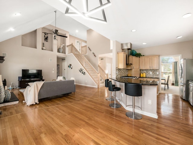 kitchen featuring dark countertops, light brown cabinets, wall chimney range hood, a breakfast bar, and freestanding refrigerator