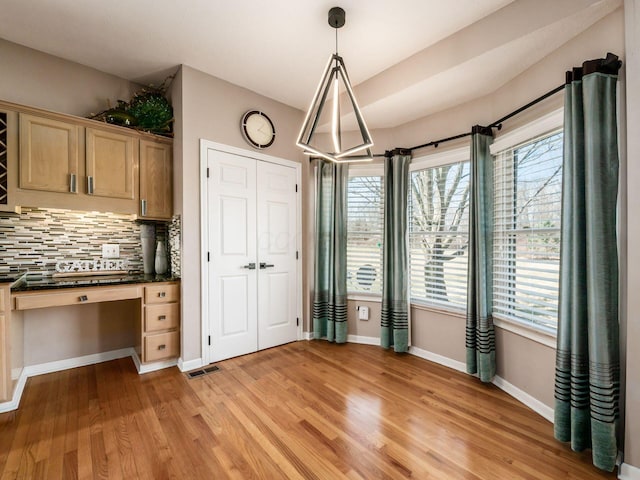 unfurnished dining area with built in desk, visible vents, baseboards, and light wood-style floors