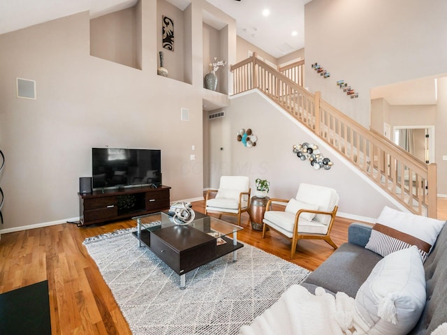 living area with baseboards, stairs, recessed lighting, a towering ceiling, and wood finished floors