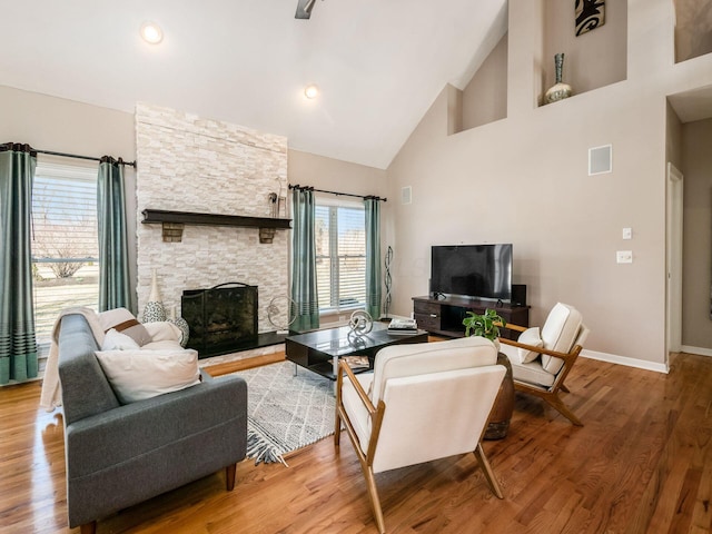 living area with wood finished floors, visible vents, baseboards, high vaulted ceiling, and a fireplace