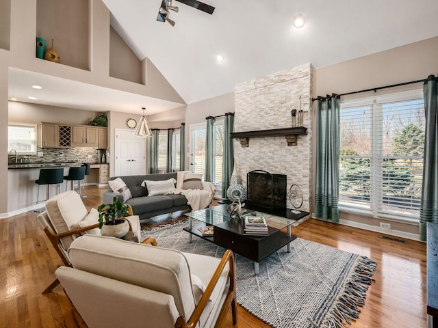 living area with a ceiling fan, visible vents, light wood finished floors, high vaulted ceiling, and a fireplace