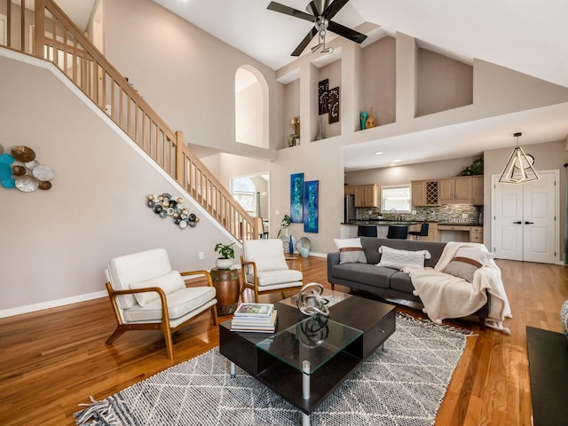 living room with ceiling fan, baseboards, light wood-style flooring, and stairs