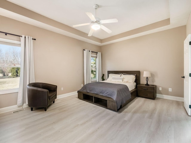 bedroom with visible vents, light wood-style flooring, a ceiling fan, a tray ceiling, and baseboards